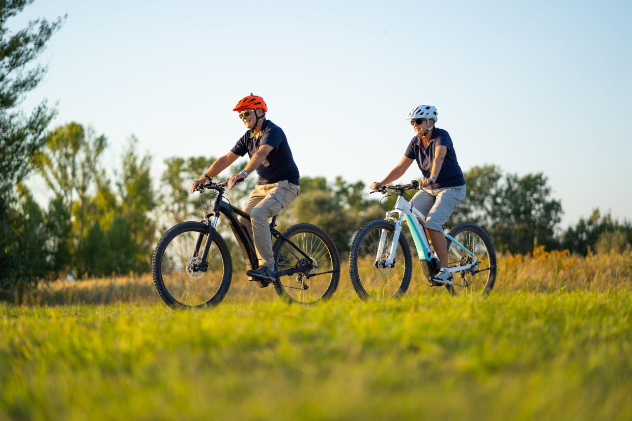 happy senior couple cycling through nature reserve on their modern electric bicyles mountain bikes on sunny summer day
