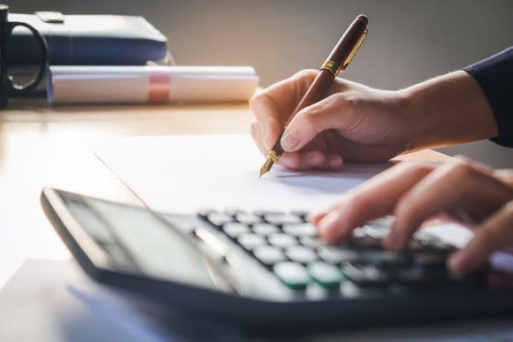 Man taking notes while typing on calculator.