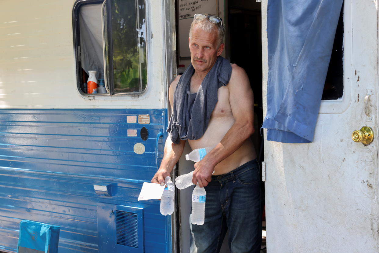 A man stands in the doorway of an RV and holds several bottles of water.