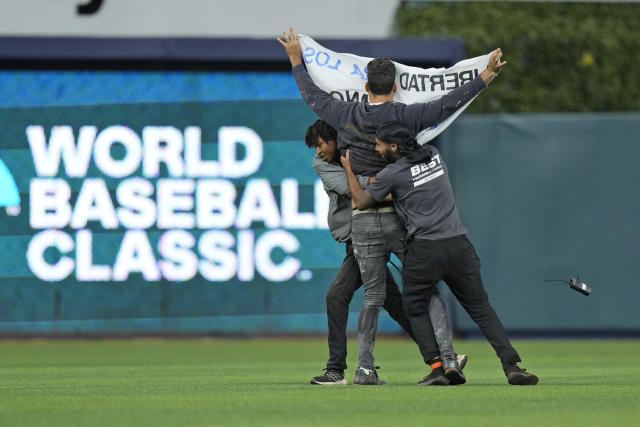 Security guards take out a demonstrator that ran onto the field during the sixth inning of a World Baseball Classic game between Cuba and the U.S., Sunday, March 19, 2023, in Miami. (AP Photo/Wilfredo Lee)