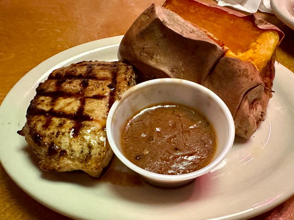 Grilled pork chop on plate with sweet potato and cup of sauce at Texas Roadhouse