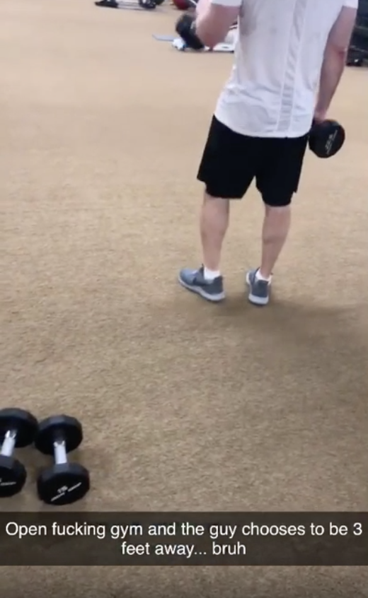 A person in a gym holding a dumbbell, with another dumbbell on the floor. Text reads: "Open fucking gym and the guy chooses to be 3 feet away... bruh"