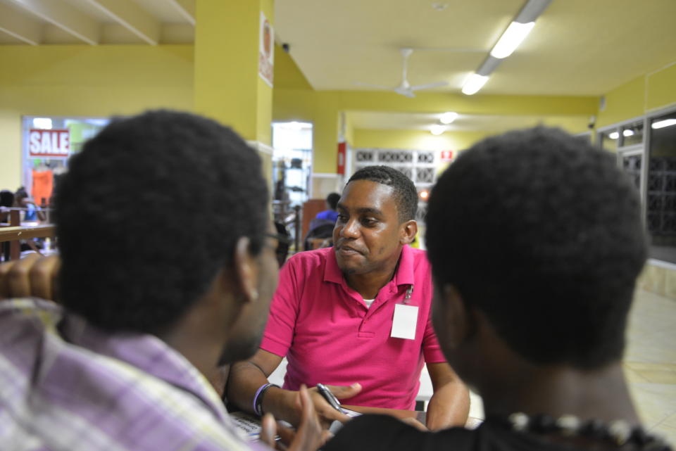 In this, April 25, 2014, photo, gay rights activist James Burton, center, of the Color Pink Group, chats with a group of young homosexual men about HIV and health issues at a shopping mall in Kingston, Jamaica. Gay sex and prostitution is illegal in Jamaica, and LGBT people who sell sex face arrest or worse. But this normally wary group is welcoming a recent outreach as a volunteer reaches out to tthem with health advice. (AP Photo/David McFadden) - JAMAICA OUT