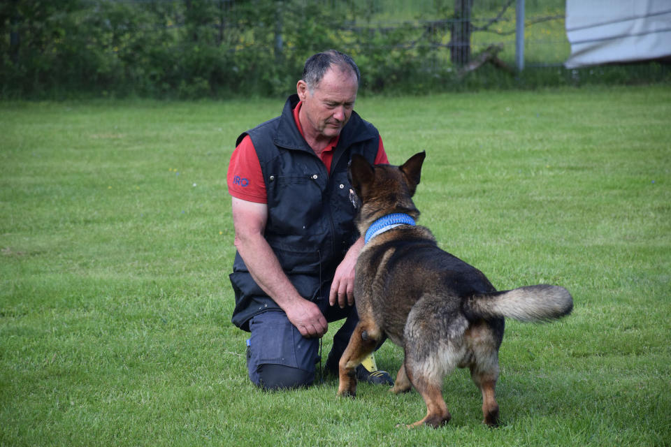 A man in a vest training a rescue dog in an open field