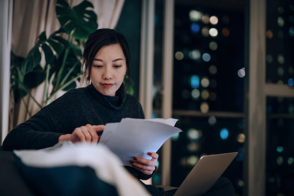 Young Asian woman handling personal finance with laptop. She is making financial plan and planning budget as she go through her financial bills, tax and expenses at home. Wealth management, banking and finance concept