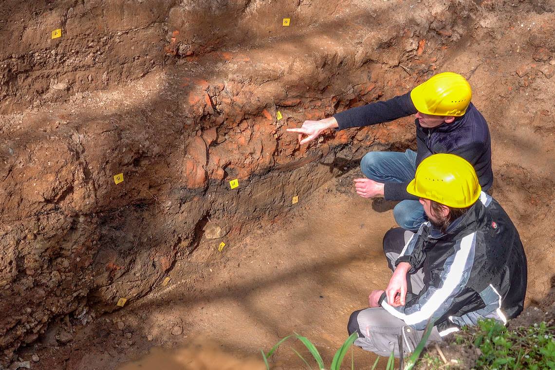 Archaeologists study traces of a burnt building in the soil layer.