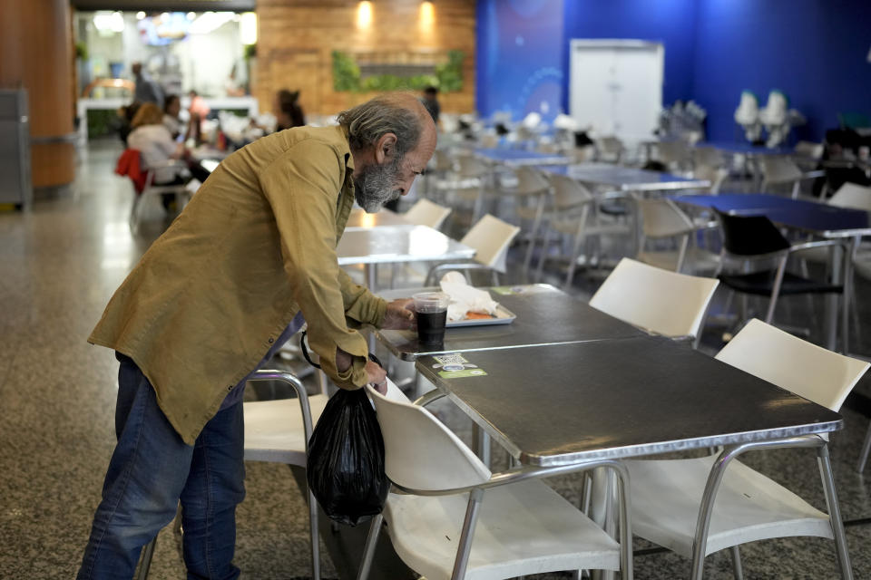 Angel Gomez picks up a beverage left on a table at the Jorge Newbery international airport, commonly known as Aeroparque, in Buenos Aires, Argentina, Thursday, April 6, 2023. Gomez, who is homeless, has made Aeroparque his home where he sleeps each evening. (AP Photo/Natacha Pisarenko)