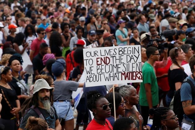 A sea of protesters fills the frame. The camera focuses on a sign that says "Our lives begin to end the day we become silent about what matters."