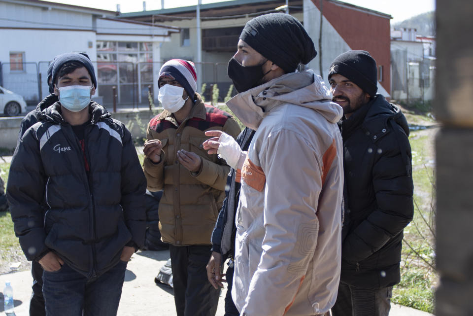 Migrants, some wearing masks for protection aganst the COVID-19 infection, speak outside the Miral camp, in Velika Kladusa, Bosnia, Wednesday, April 7, 2021. Bosnia is seeing a rise in coronavirus infections among migrants and refugees living in its camps, as it struggles to cope with one of the Balkans' highest COVID-19 death and infection rates among the general population.(AP Photo/Davor Midzic)