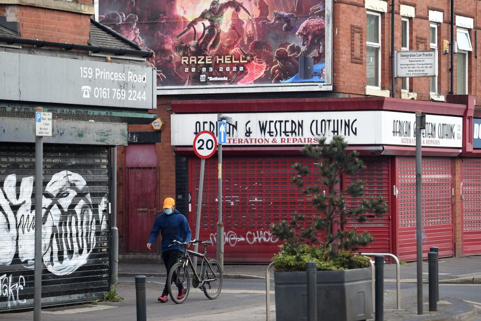 A man wearing a protective face mask wheels his bicycle past shuttered shops in Manchester, north-west England on May 11, 2020, as life in Britain continues during the nationwide lockdown due to the novel coronavirus pandemic. - The British government on Monday published its plan to ease the nationwide coronavirus lockdown in phases in England, with some schools and shops opening from June and recommending people wear face masks in some settings. (Photo by Oli SCARFF / AFP) (Photo by OLI SCARFF/AFP via Getty Images)