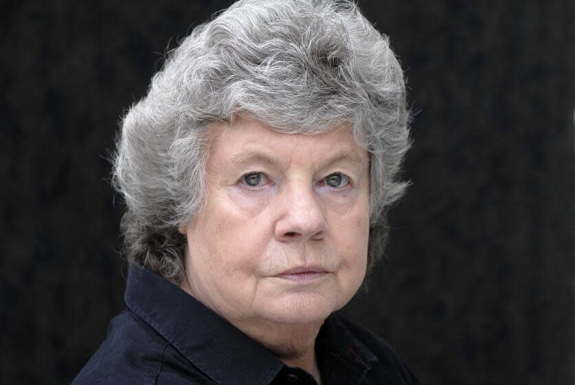 A closeup image of a woman with short grey hair looking ahead and posing against a black backdrop