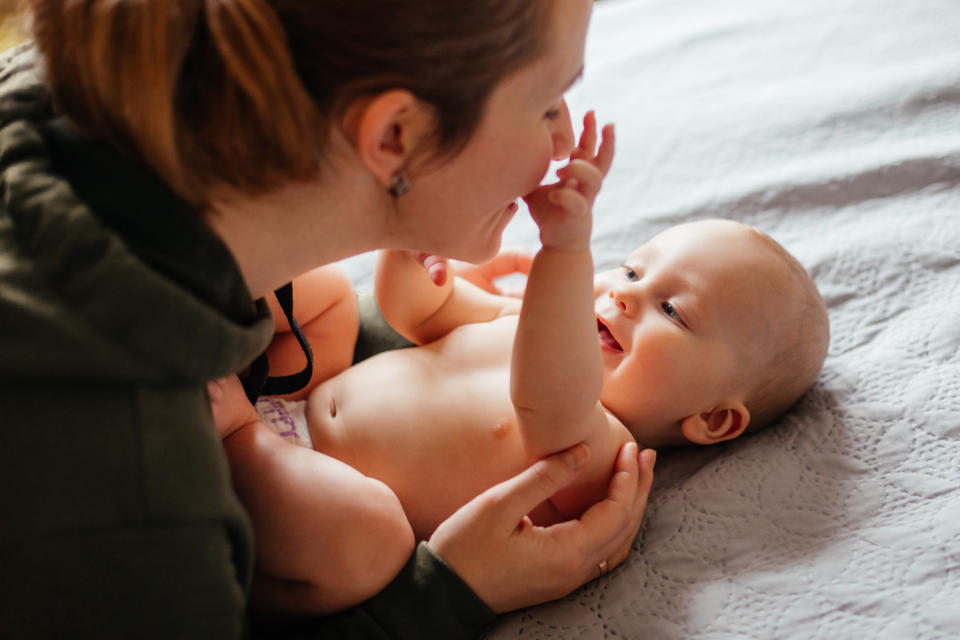 Woman interacting with a happy baby lying on a bed