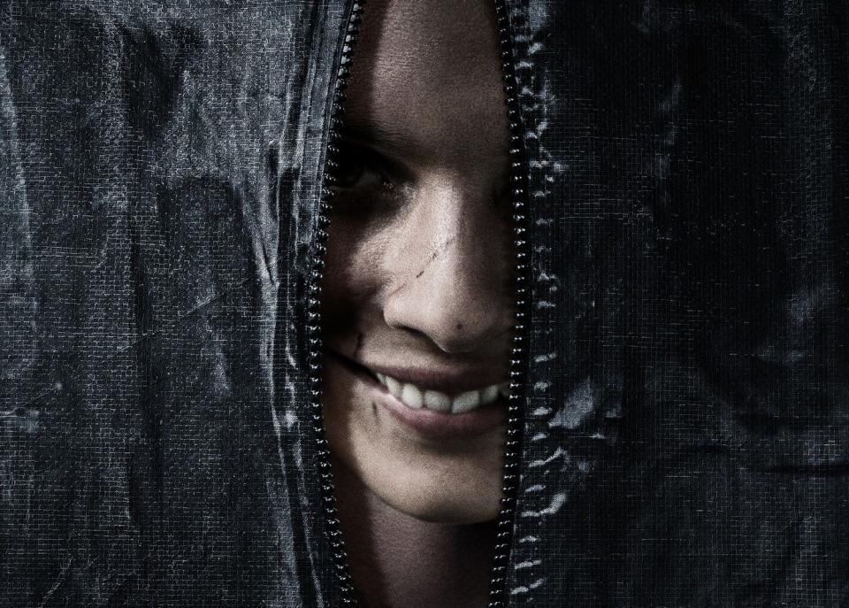 A creepy smiling face in peering out of an unzipped body bag from the movie poster for "Smile."