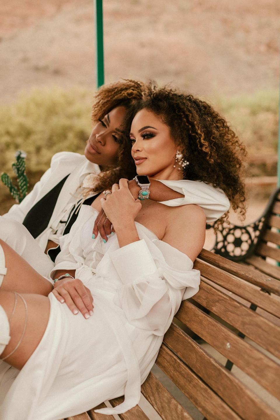 Two brides sit on a bench in the desert.