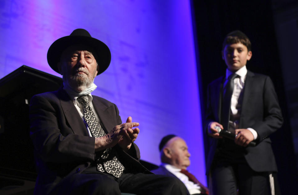 Aharon Wolf, 89, left, and David Einhorn, 95, center, sit on stage while Orthodox Jewish singer Yaakov Shwekey and young talent Nz Zlotowitz, right, perform a concert for them and other Holocaust survivors on Monday, June 14, 2021, at the Yeshivah of Flatbush theater at Joel Braverman High School in the Brooklyn borough of New York. It was the first large gathering for New York-area Holocaust survivors after more than a year of isolation due to the coronavirus pandemic. (AP Photo/Jessie Wardarski)