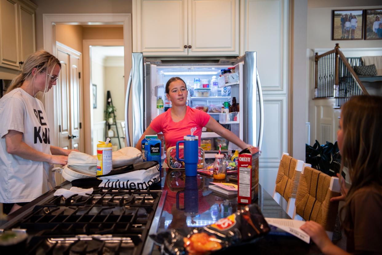 Haley Eason sanitizes the laptops from school while her daughter Myleigh, 11, opens the fridge to look for a drink, Madelyn, 9, opens her book to beginning some light reading at home in Spring Hill, Tenn., Monday, April 15, 2024.