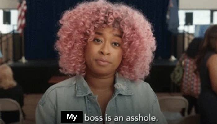 A woman with curly hair and a denim jacket stares straight ahead with a neutral expression. Text on the image reads, "Your boss is an asshole."