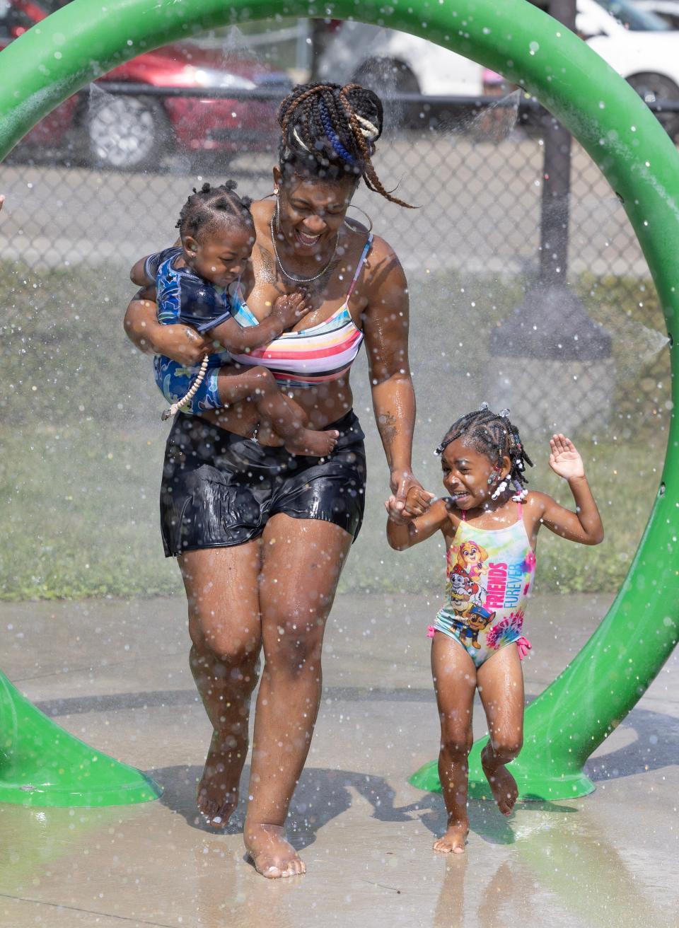 Donisha Jones runs through a water fountain Thursday, July 13, 2023, with her children, Novah Jones, 3, and Justin Johnson, 1, at the Crenshaw Park spray park in Canton.