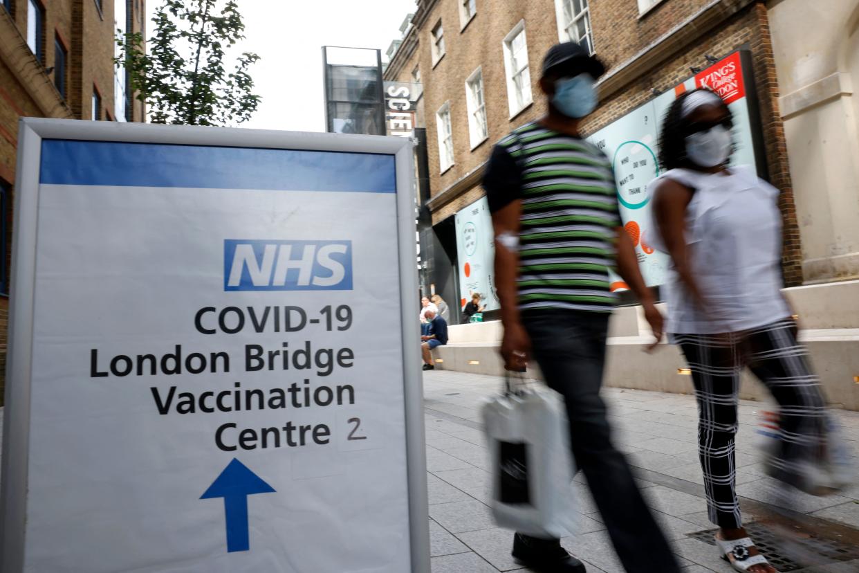 People pass signs indicating the entrance to the London Bridge Vaccination Centre in London on August 9, 2021. - After updated guidance from British health regulators, coronavirus vaccinations have been extended to those aged 16 and 17 without underlying health issues, but not to younger healthy teenagers as in many other Western countries. (Photo by Tolga Akmen / AFP) (Photo by TOLGA AKMEN/AFP via Getty Images)