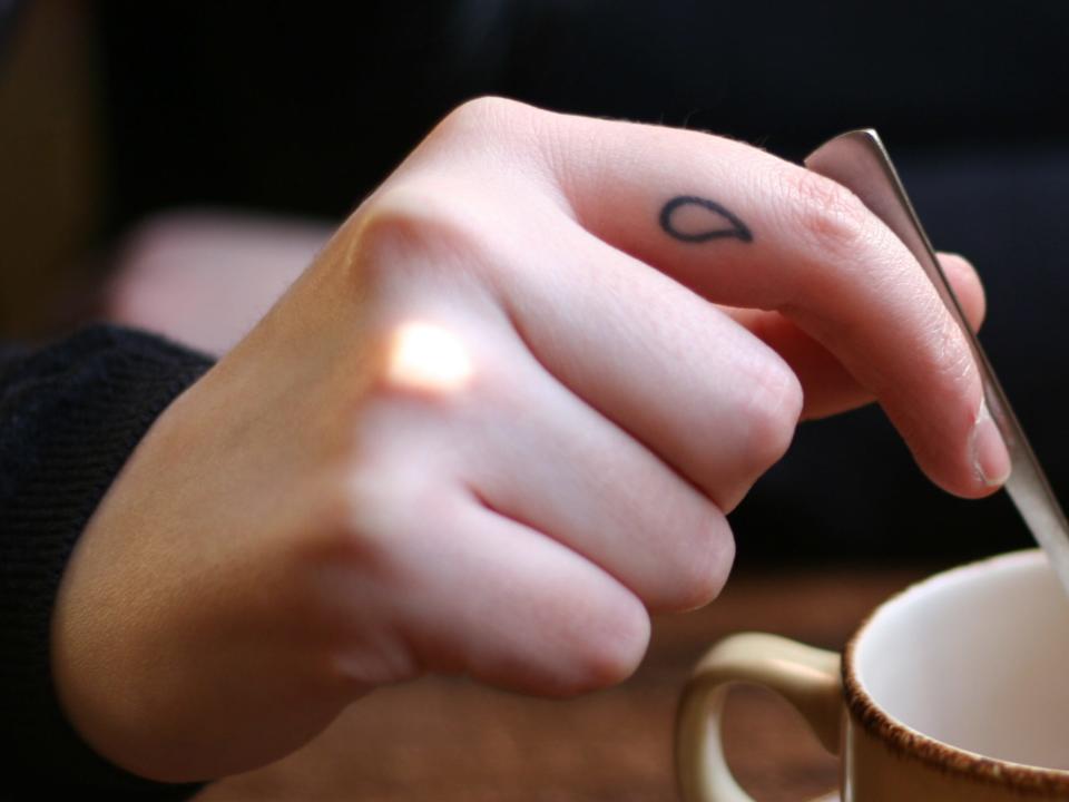 person stirring a coffee with a raindrop finger tattoo