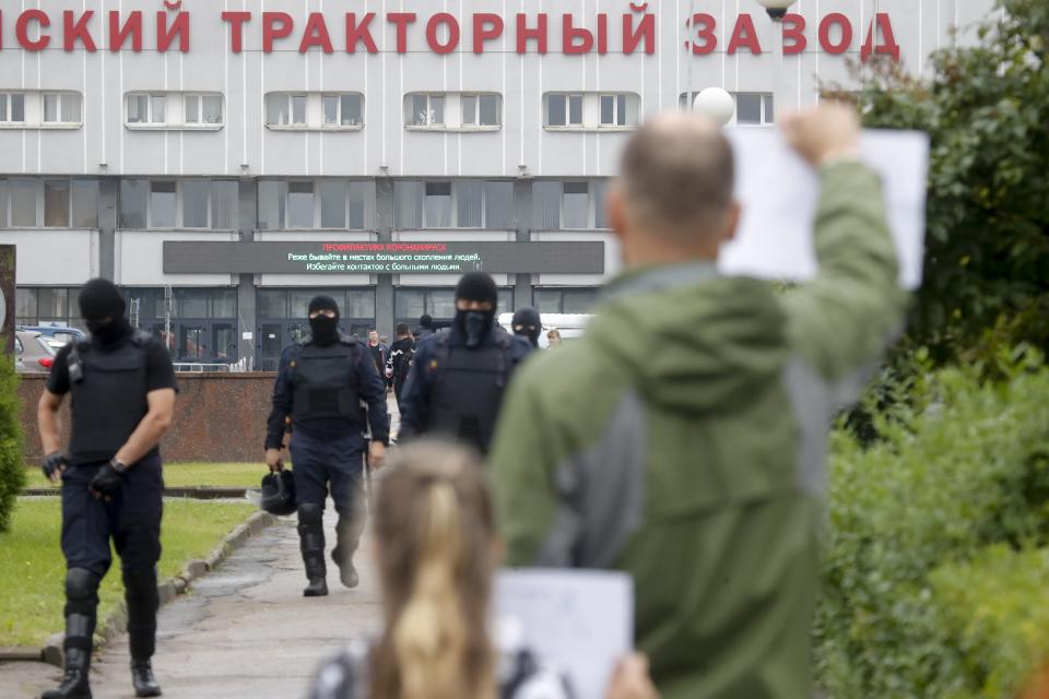 Protesters stand in front of the Minsk Tractor Works Plant holding posters supporting workers as police walk to push them back in Minsk, Belarus, Wednesday, Aug. 19, 2020. Workers at state-controlled companies have joined strikes this week, as the unprecedented mass protests enter their 11th day and erode the authority of the man once dubbed "Europe's last dictator." (AP Photo/Dmitri Lovetsky)