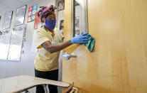 FILE - In this July 14, 2020, file photo, amid concerns of the spread of COVID-19, Alma Odong wears a mask as she cleans a classroom at Wylie High School in Wylie, Texas. The cost of bringing students back to classrooms is proving a major stumbling block to safely reopening schools across the U.S. (AP Photo/LM Otero, File)