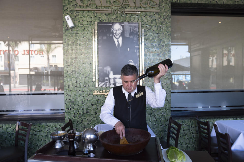 Salad Master Efrain Montoya prepares a Caesar salad in front of an image of the inventor of the salad, Caesar Cardini, at Ceasar's restaurant Thursday, June 27, 2024, in Tijuana, Mexico. Caesar salad has something to celebrate: It's turning 100. Italian immigrant Caesar Cardini is said to have invented the dish on July 4, 1924, at his restaurant, Caesar's Place, in Tijuana, Mexico. (AP Photo/Gregory Bull)