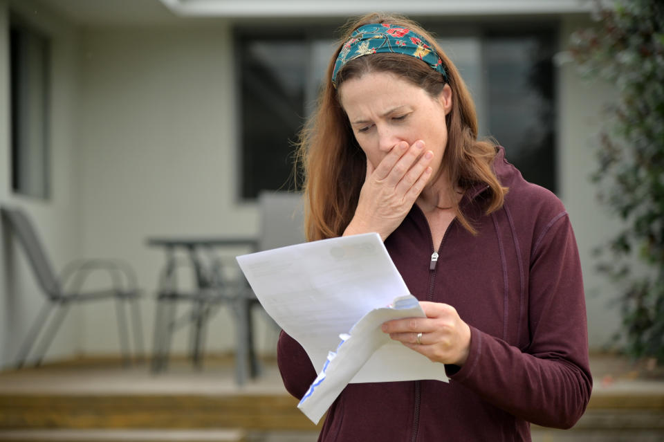 An upset woman reading a letter from a payday lender in her home front yard.