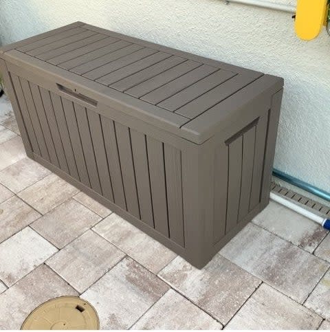 Outdoor storage bench made of resin with a flat lid and vertical slats, suitable for patio use