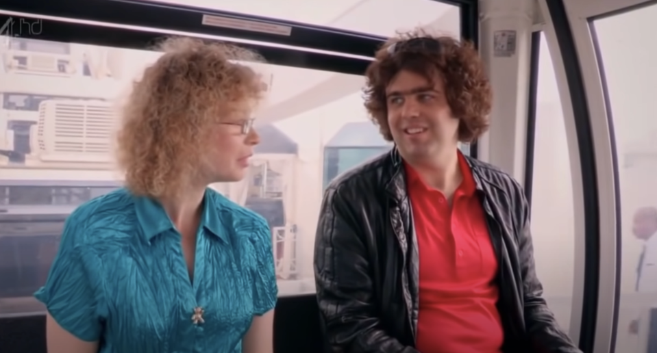 A woman and a man sit inside a cabin, likely a ferris wheel, both appearing cheerful and engaged in conversation