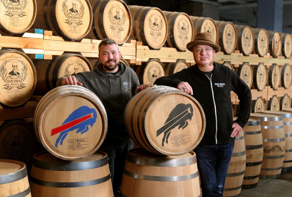 Tommy Brunett, an owner at Iron Smoke Distillery (right) and Drew Wescott, master distiller, with two barrels of bourbon they put up in 2016 after a visit by Buffalo Bills staff during training camp.