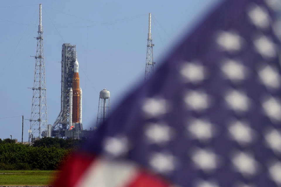 FILE - An American flag flies in the breeze as NASA's new moon rocket sits on Launch Pad 39-B after being scrubbed at the Kennedy Space Center Sept. 3, 2022, in Cape Canaveral, Fla. It’s not just rocket fuel propelling America’s first moonshot after a half-century lull. Rivalry with China’s space program is helping drive NASA’s effort to get back into space in a big way. That's as both nations push to put people back on the moon and establish the first lunar bases. (AP Photo/Chris O'Meara, File)