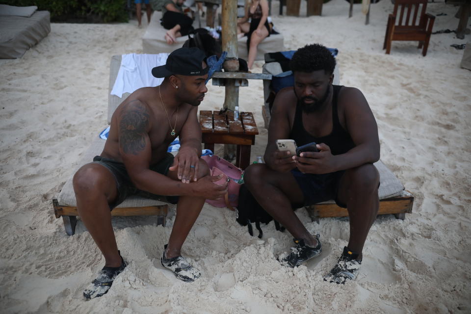 U.S. tourists Latron Evans, left, and Gearald Green, check their phones at a beach in Tulum, Quintana Roo state, Mexico, Monday, Jan. 4, 2021. The friends from Jackson, Mississippi, relaxed on lounge chairs and romped in the Caribbean waters, grateful for a break from the new coronavirus pandemic winter in the United States. (AP Photo/Emilio Espejel)