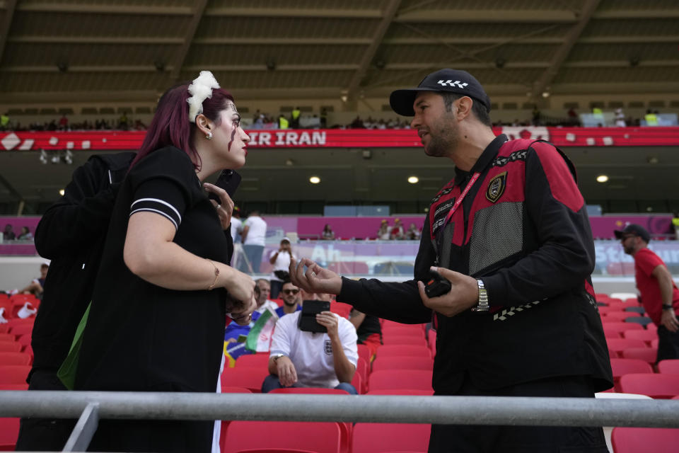 A member of security, right, interacts with an Iran supporter who displayed a shirt that read 'Mahsa Amini 22' in memory of an Iranian woman who died while in police custody in Iran, prior to the start of the World Cup group B soccer match between Wales and Iran, at the Ahmad Bin Ali Stadium in Al Rayyan, Qatar, Friday, Nov. 25, 2022. (AP Photo/Alessandra Tarantino)