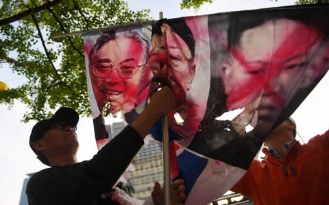 A conservative activist prepares to display partially burnt images of late North Korean leaders Kim Il Sung (L), Kim Jong Il  - Credit: AFP