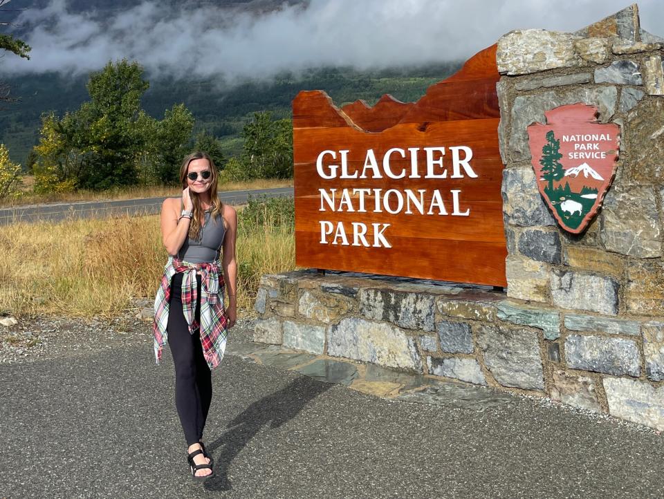 A woman standing in front of the Glacier National Park sign.