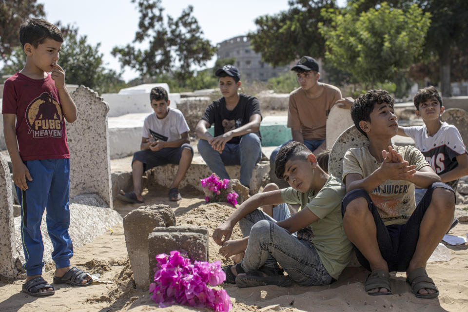 Relatives of the children of the Nijim family, who were killed in an Israeli raid, sit around their graves at Al-Faluja cemetery in Jabalia, in the northern Gaza Strip, Tuesday, Aug 8, 2022. A Palestinian human rights group and an Israeli newspaper reported Tuesday that an explosion in a cemetery that killed five Palestinian children during the latest flare-up in Gaza was caused by an Israeli airstrike and not an errant Palestinian rocket. (AP Photo/Fatima Shbair)