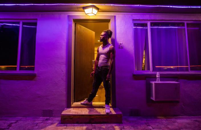 A man stands in a doorway cast in a purple-pink light