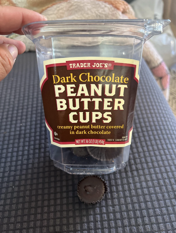 Hand holding a container of Trader Joe's Dark Chocolate Peanut Butter Cups with one piece visible