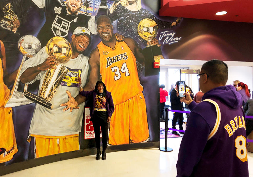 Janel Alexander, 55, of Encino, poses next to a mural that features Kobe Bryant and Shaquille O'Neil inside Staples Center in Los Angeles before a public memorial for Lakers legend Bryant and his daughter Gianna Monday morning, Feb. 24, 2020. Alexander said she wanted to attend the memorial to support Bryant's wife, Vanessa, so she could feel "the presence of love around her." (AP Photo/Stefanie Dazio)