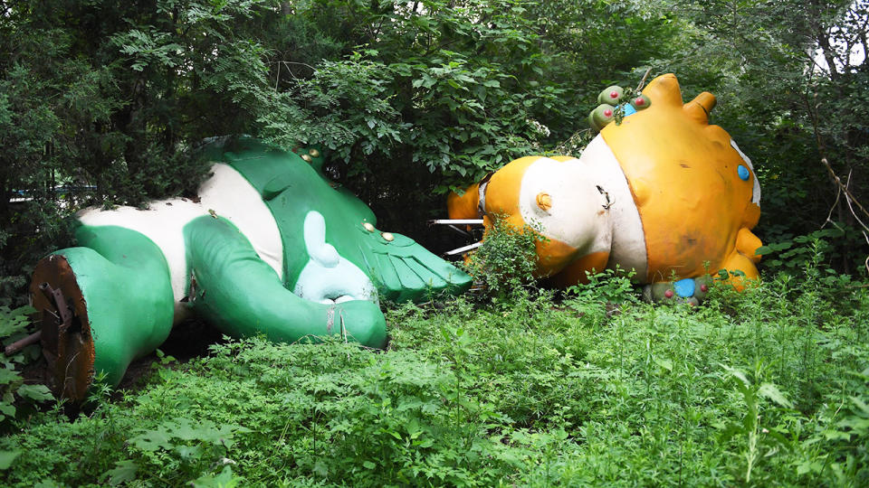 Two of the five mascots for the Beijing Olympics lying among trees behind an abandoned, never-completed mall.