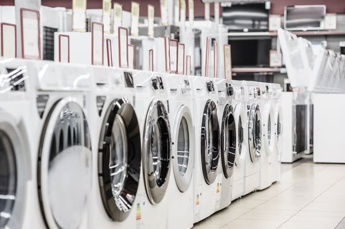 A row of shiny washing machines in an appliance store.
