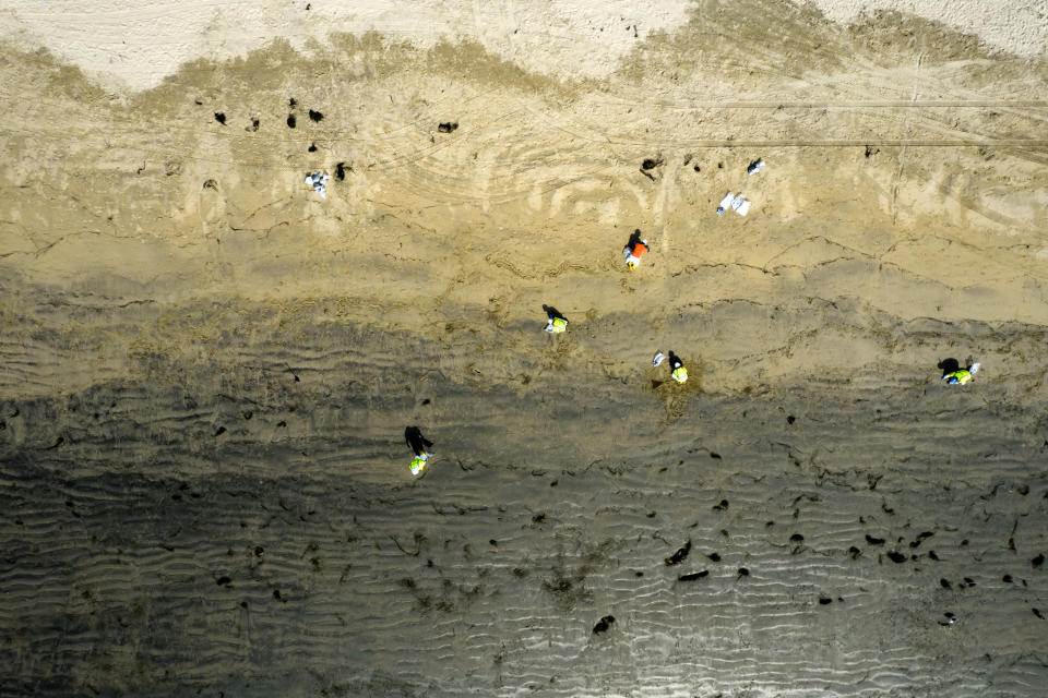 In this aerial image taken with a drone, workers in protective suits clean the contaminated beach after an oil spill in Newport Beach, Calif., on Wednesday, Oct. 6, 2021. Some of the crude oil that spilled from a pipeline into the waters off Southern California has been breaking up naturally in ocean currents, a Coast Guard official said Wednesday as authorities sought to determine the scope of the damage. (AP Photo/Ringo H.W. Chiu)