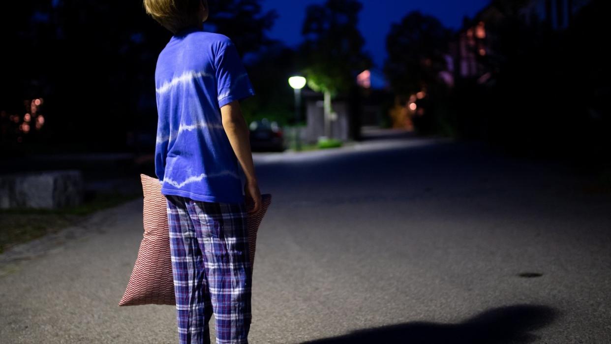 Im Schlafanzug steht ein Kind mit einem Kissen in der Hand nachts auf einer Straße. Foto: Sven Hoppe/Illustration