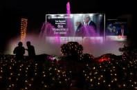 Media persons work as they stand in front of a hoarding with the images of India’s Prime Minister Narendra Modi and U.S. President Donald Trump along a road ahead of Trump’s visit, in Ahmedabad