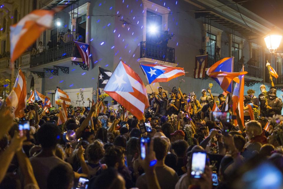 People celebrate outside the governor's mansion La Fortaleza, after Gov. Ricardo Rossello announced that he is resigning Aug. 2 after nearly two weeks of protests and political upheaval touched off by a leak of crude and insulting chat messages between him and his top advisers, in San Juan, Puerto Rico, Thursday, July 25, 2019. (AP Photo/Dennis M. Rivera Pichardo)