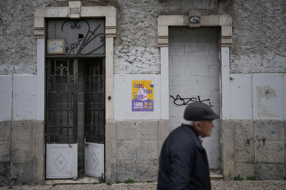 An elderly man walks by an uninhabited building near a poster announcing a protest to demand measures to deal with the housing crisis, in Lisbon, Saturday, March 11, 2023. Portugal’s center-left Socialist government is set to approve a package of measures to address the country's housing crisis. A growing number of people are being priced out of the property market by rising rents, surging house prices and climbing mortgage rates. (AP Photo/Armando Franca)