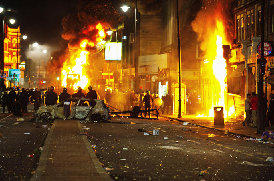 High street caught in flames with debris surrounding riot police.