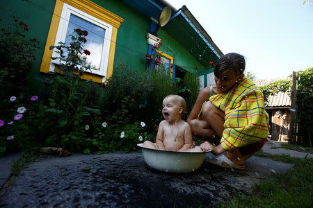 Ekaterina, a granddaughter of 75-year old Ekaterina Panchenya, bathes her daughter Dasha in a basin on a hot summer day in the village of Pogost, Belarus, August 15, 2017. For Ekaterina Panchenya, it was "cars, noise and dirt" and the sight of city-dwellers standing in line to buy groceries that dissuaded her from leaving her smallholding in the village of Pogost. REUTERS/Vasily Fedosenko