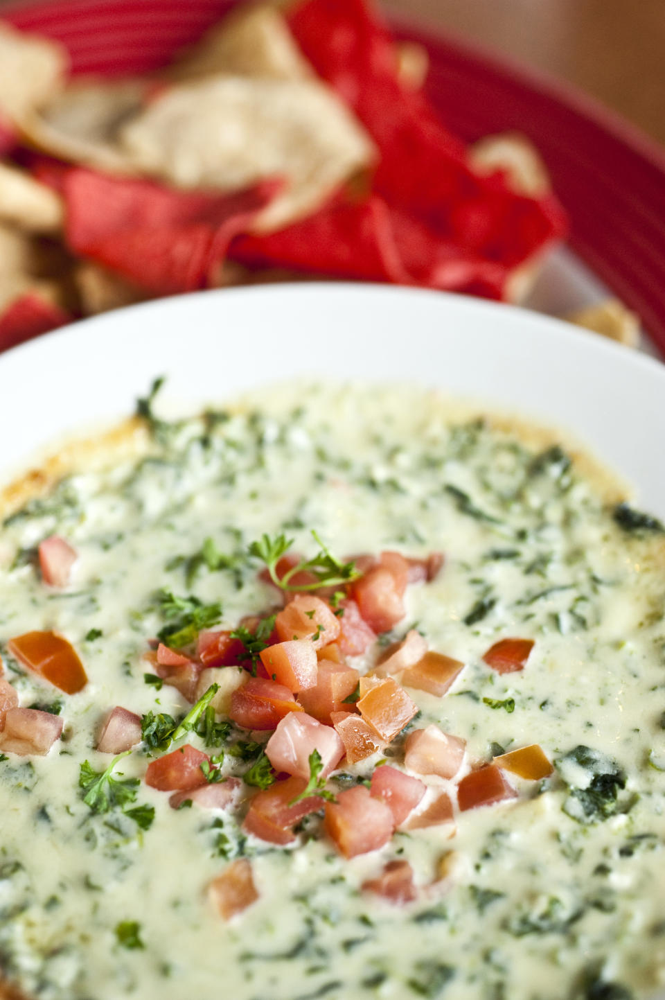 Spinach dip in a white bowl topped with diced tomatoes, served with tortilla chips